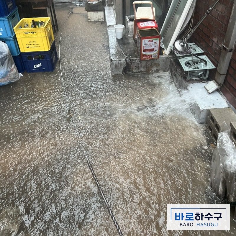 물이 고인 건물 뒤편 하수구에 스프링 케이블을 넣어 작업하는 모습