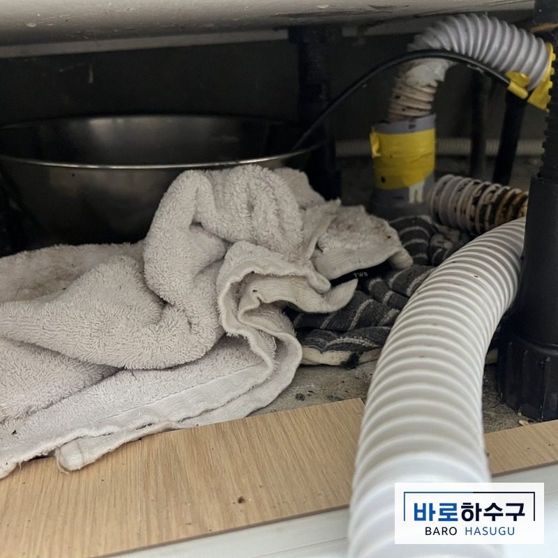 과천 부림동 현장 싱크대 하부장 안쪽, 수건이 깔린 작업 전 배관과 호스